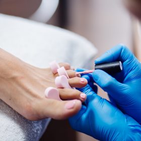 home-salon-pedicure-foot-care-treatment-nail-process-professional-pedicures-master-blue-gloves-apply-light-pink-gel-polish